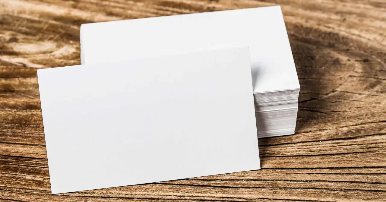 Pila de tarjetas de visita blancas sobre madera. El gramaje del papel es ideal para impresi&oacute;n profesional.