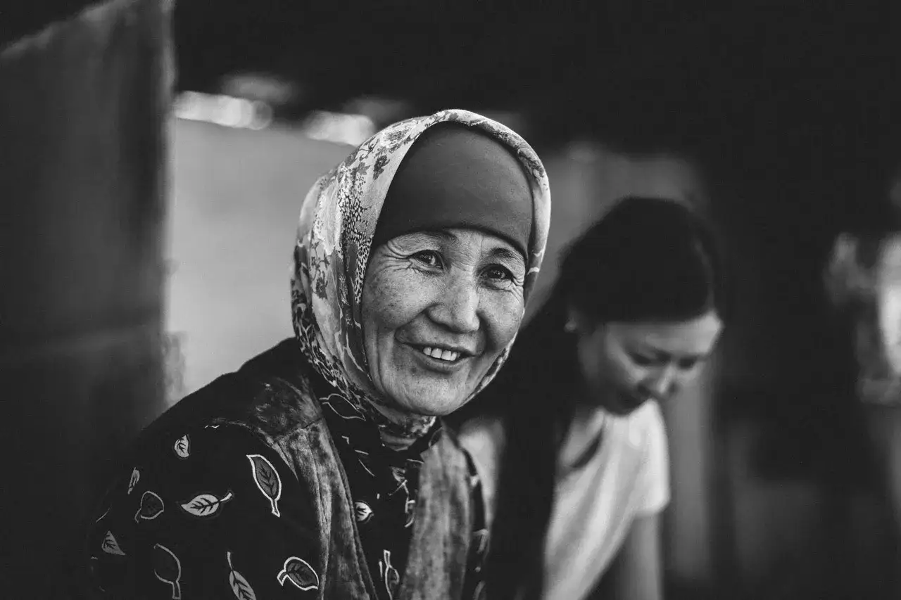 Una anciana sonr&iacute;e, su rostro arrugado cuenta fotos con historia. A su lado, una mujer joven se inclina, tambi&eacute;n parte de este relato visual.