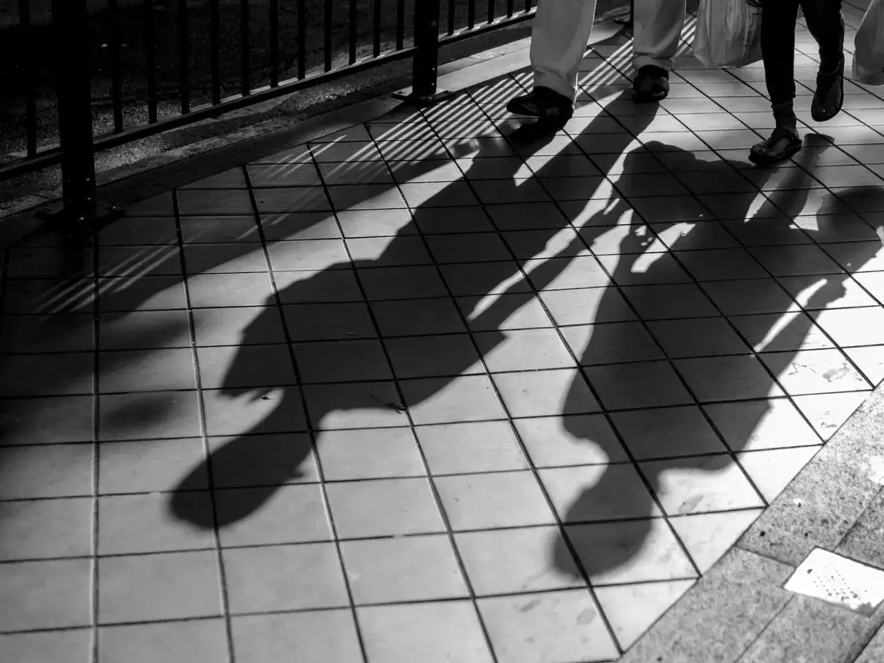Sombras alargadas de personas caminando sobre baldosas, creando fotos creativas con un juego de luces y l&iacute;neas.